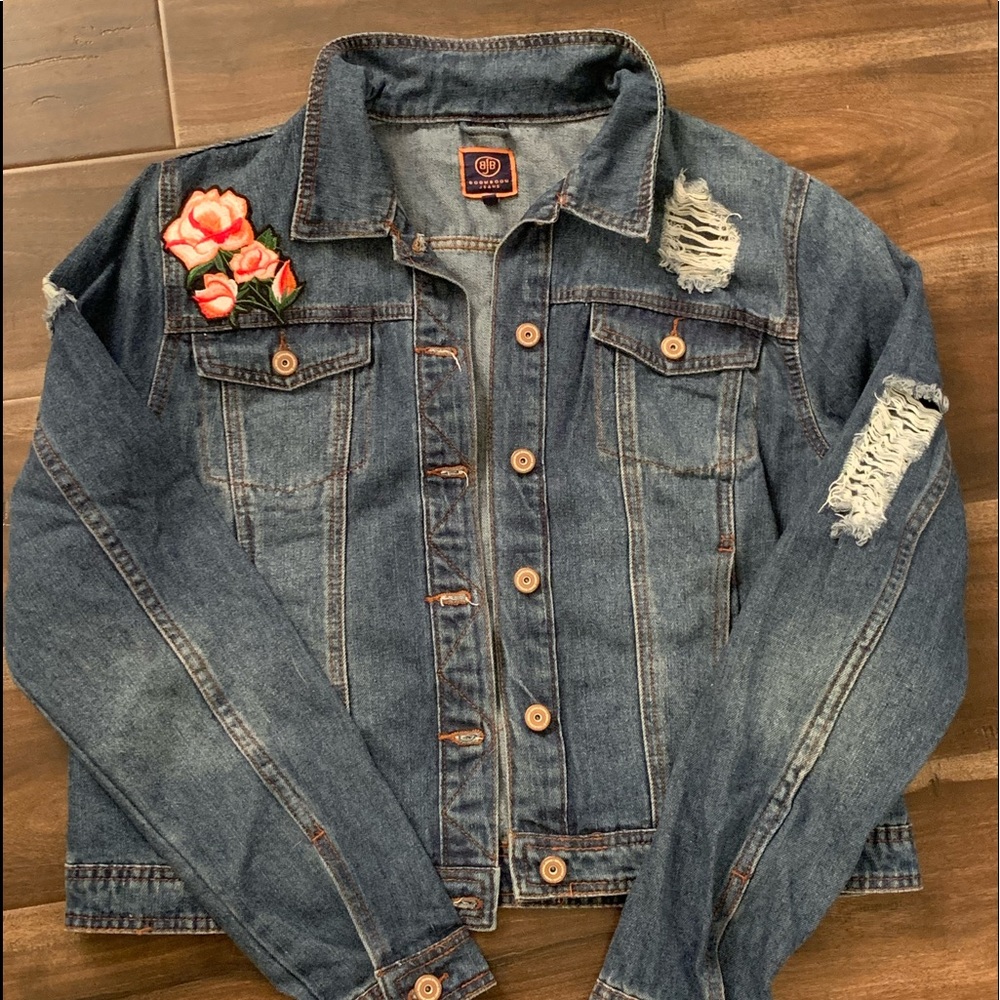 A blue jean jacket with rips and a rose pattern